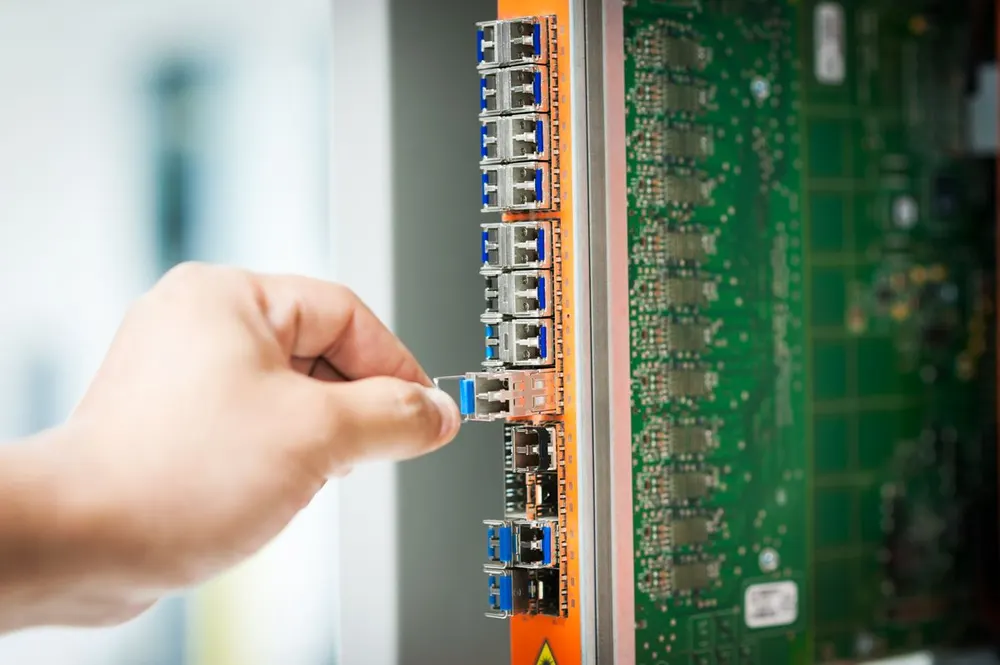 Hand prüft eine Glasfaser-Steckverbindung an aktiver Netztechnik